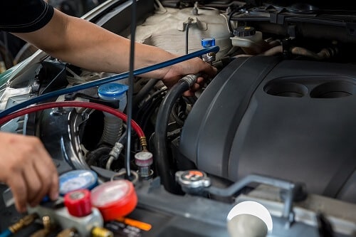 Air Conditioning/Heating Service in Gilbert, AZ | Ace Performance Auto. Closeup image of an auto mechanic checking and fixing a car’s air conditioner system in a car garage. 