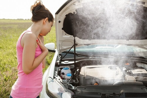 What to do with Engine Overheating | Ace Performance Auto in Gilbert, AZ & Queen Creek, AZ. Image of a frustrated young woman looking at the overheated engine of her car on the road.